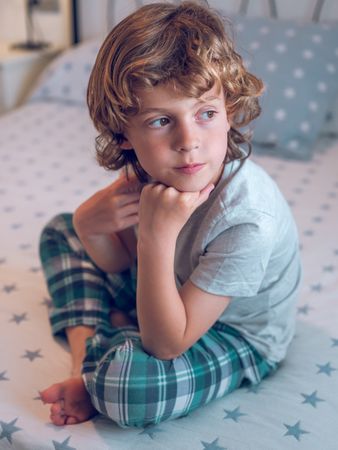 Cute little boy sitting with crossed legs in bed