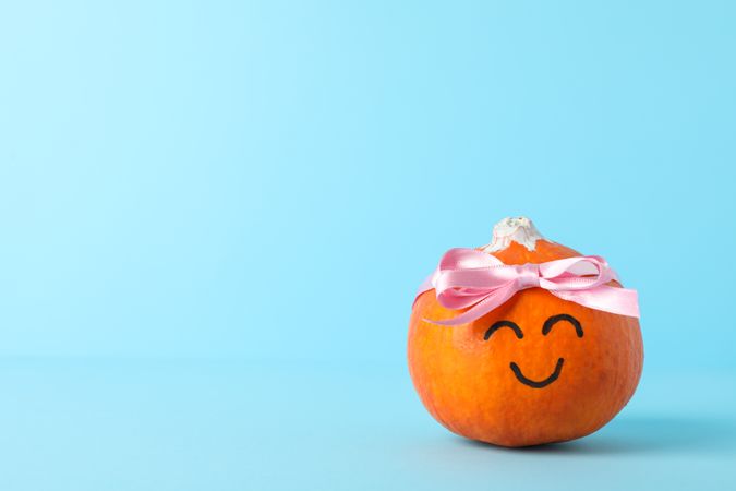Happy pumpkin with bow on blue background, space for text