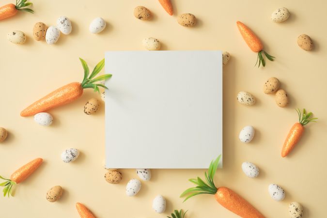 Easter eggs and carrots on pastel yellow background with paper card note