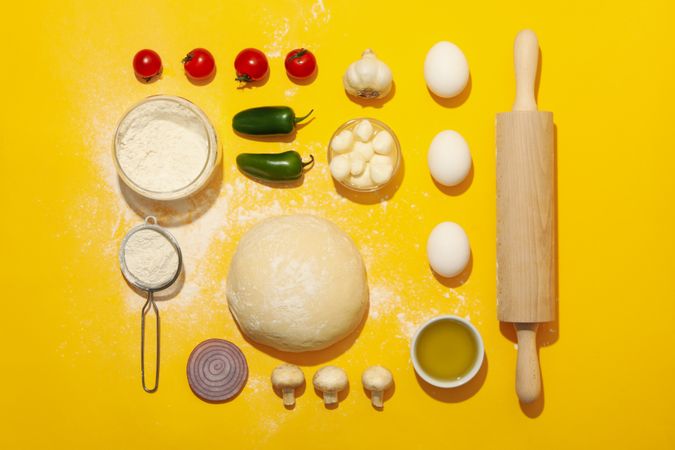 Dough and ingredients for cooking pizza on yellow background