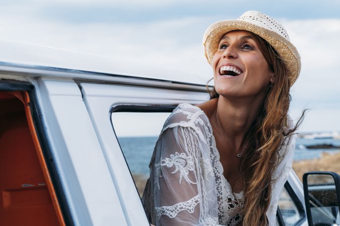 Smiling woman in hat in front seat of car opening door