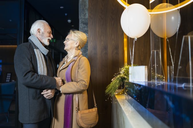 Cute mature couple standing at front desk of hotel with balloons