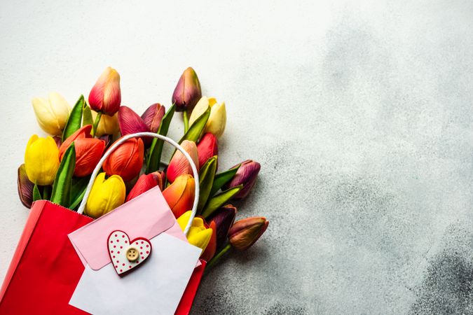 Tulips in shopping bag with present and pink envelope on grey counter
