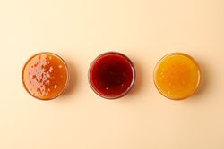 Bowls with jam on beige background, top view