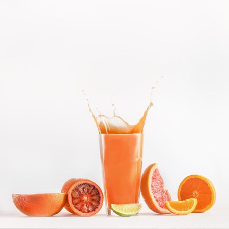 Splashing of citrus juice in glass with blood orange, grapefruit and lime. Refreshing healthy drink with vitamins. Liquid in motion. Front view.
