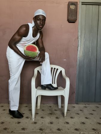Young man holding watermelon putting one leg on plastic chair