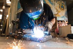 Welder in protective helmet welding metal detail in workshop