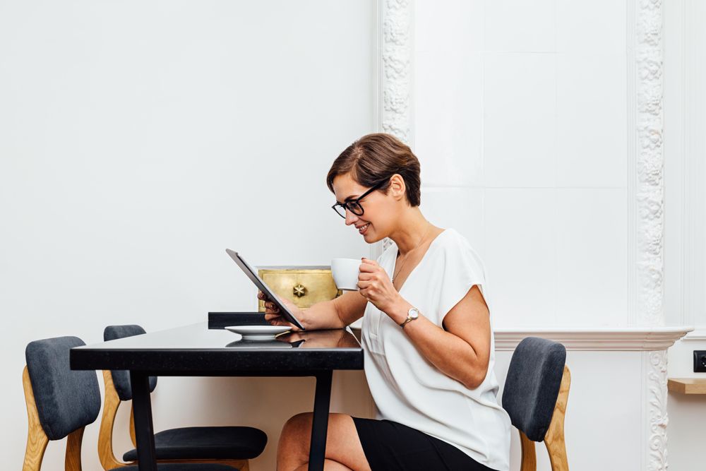 Smiling woman reading on her tablet with a coffee