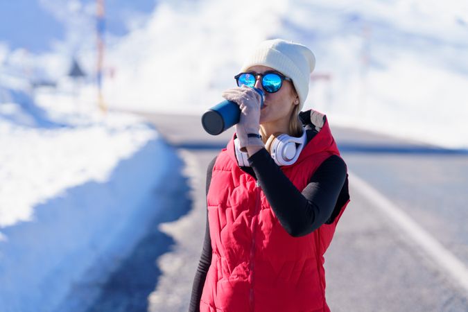 Woman in wintry gear sipping from thermos in the mountains on cold day