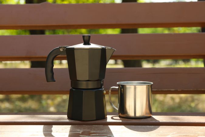Coffee maker and metal cup on bench outdoor