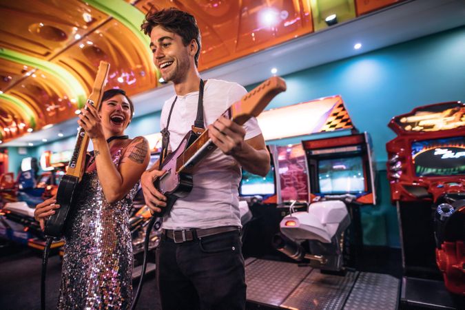 Couple playing the guitar game holding gaming guitars at a gaming parlour
