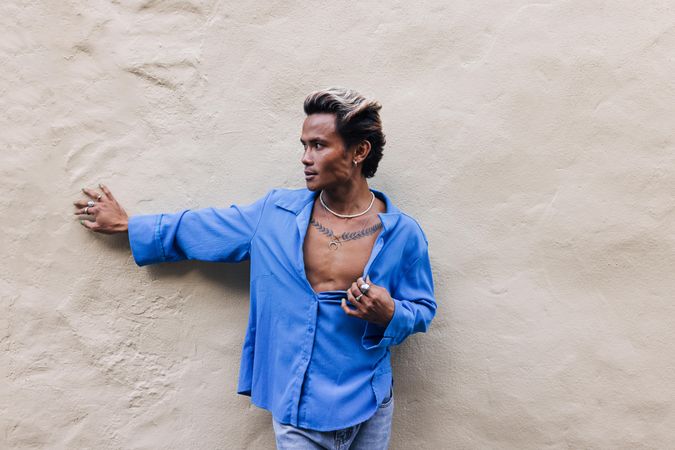 Male in blue shirt and jeans leaning against wall and looking away