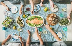 Group of people serving themselves fish, on blue patterned table with wine and side dishes and bread