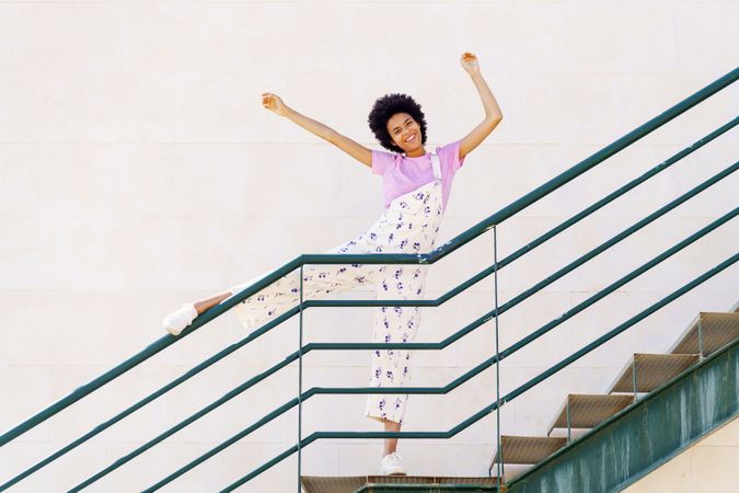 Elated woman on stairs with leg up on green handrail and arms up