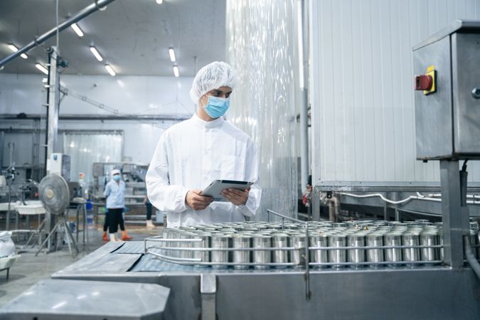 Researcher inspecting canned food processing on conveyor belt at fish factory