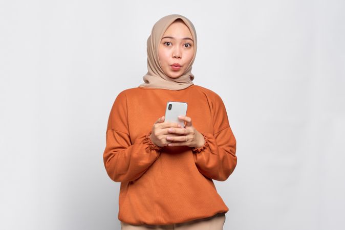 Concerned Muslim woman in headscarf and orange shirt holding phone