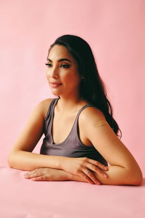 Pensive Hispanic woman looking away from camera and sitting in pink room, vertical
