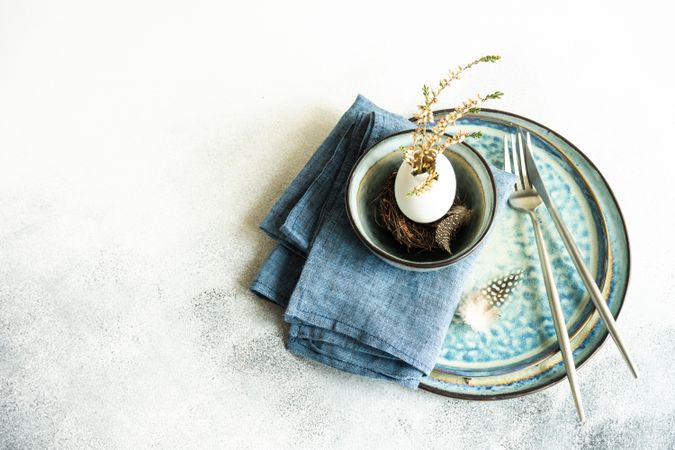 Easter table setting with decorative egg shell, feather and heather on blue plates with copy space