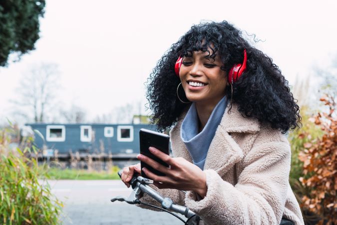 Delighted Black woman with smartphone on bicycle