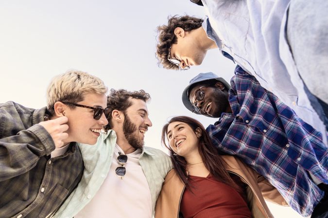 Happy diverse group of young friends in a circle smiling outdoors under blue sky in sunny day