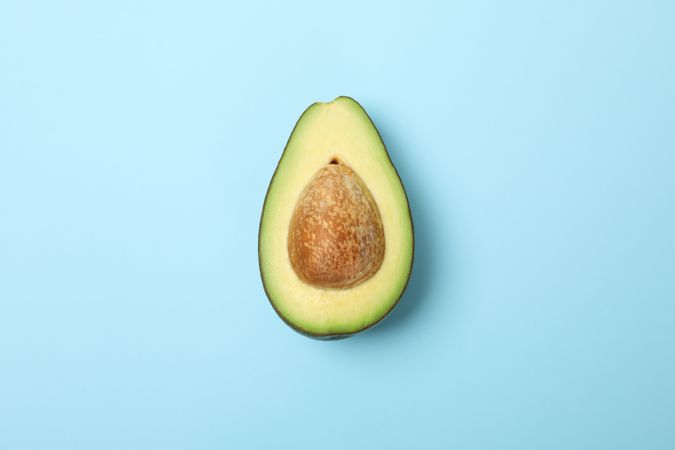 Half of fresh avocado on blue background, space for text