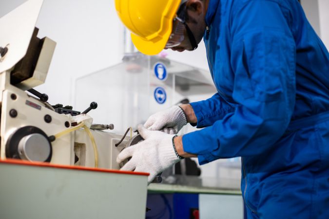 Male in blue jumpsuit and PPE gear operating controller in manufacturing factory