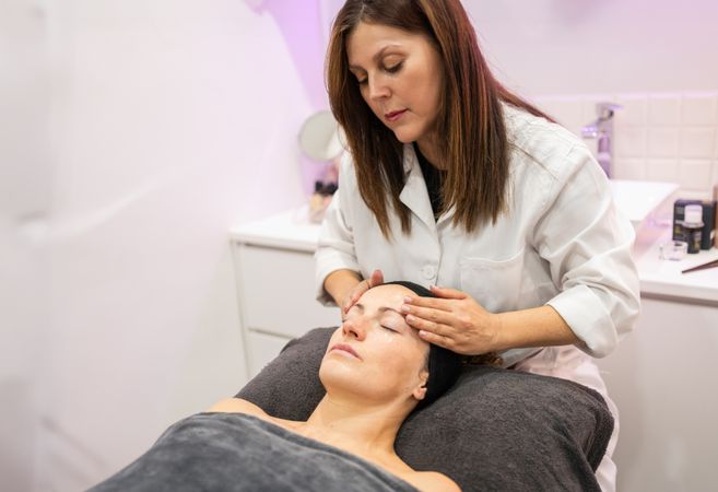 Beautician massaging face of female client in beauty salon