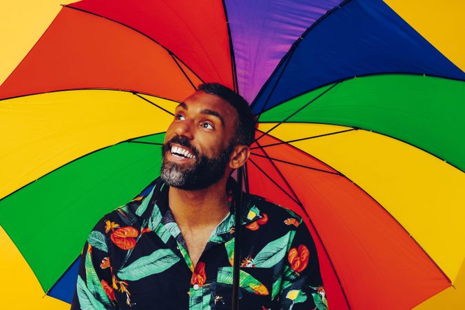 Smiling man looking up from under colorful umbrella