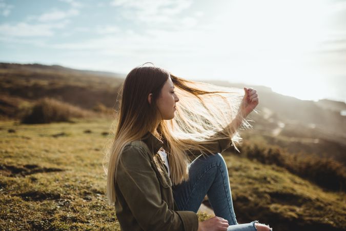 Pensive woman sitting on grass and looking at seascape