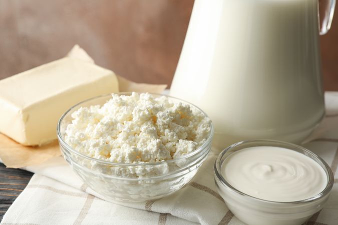 Milk, cottage cheese and butter against brown background, closeup
