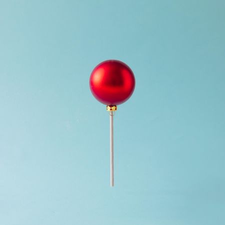 Lollipop made of red Christmas bauble on blue background