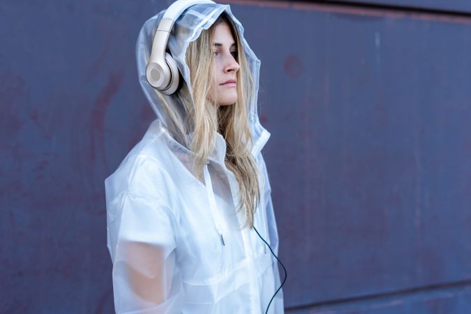 Pensive stylish woman in raincoat with headphones