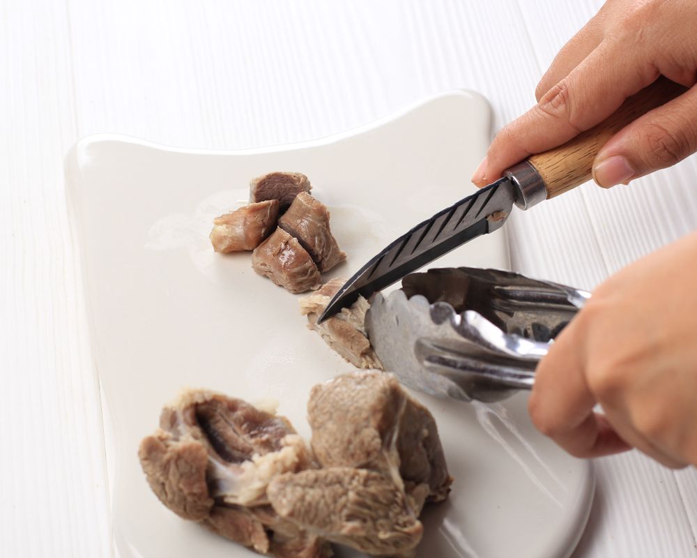Person cooking beef into chunks