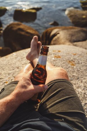 Bottle of beer in hand with seascape on background