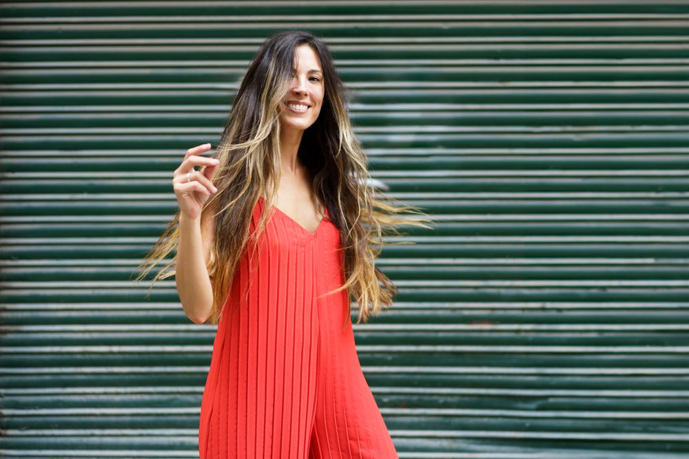 A Joyful Woman Dressed in a Vibrant Red Dress Posing Gracefully Against a Lively Green Backdrop