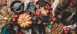 Thanksgiving table setting for gathering with woman serving roast chicken plate, wide composition