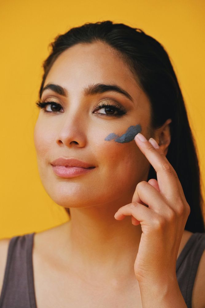 Confident Latina woman applying clay mask with hand