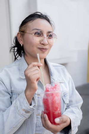 A young Hispanic woman is smiling while drinking a Mexican cherry slushy outdoors