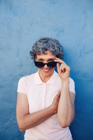 Portrait of attractive woman peeking over sunglasses against blue wall