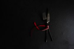 Dark knife and fork on dark background tied with bright red ribbon