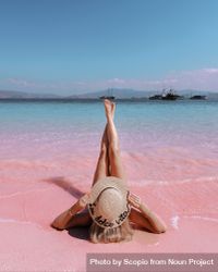 Woman in brown sun hat lying on pink beach in Indonesia 0VxwY4