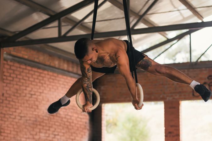 man athlete training in gymnastic rings doing a straddle planche
