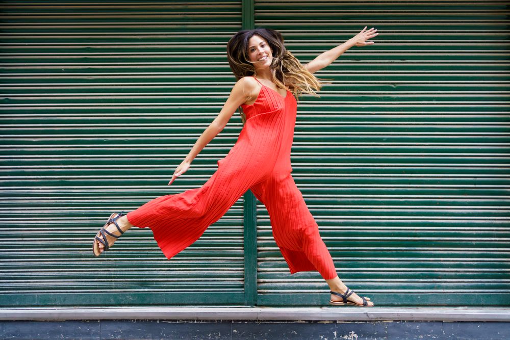 A Joyful Woman in a Red Jumpsuit Dances Playfully Against a Lively Green Background