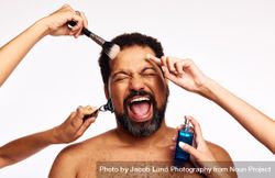 Hands of women shaving, applying makeup and cologne to excited bearded person 5nVND5