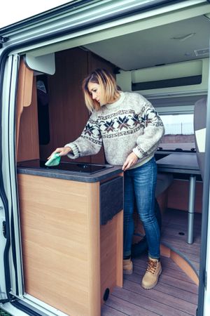 Woman in warm sweater cleaning while standing in back of van, vertical