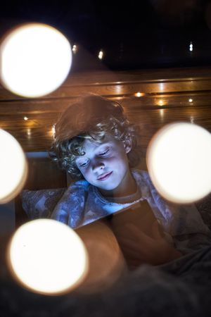 Boy surfing tablet in cozy lights