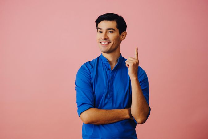 Medium shot of Latino man in pink studio with finger pointed up