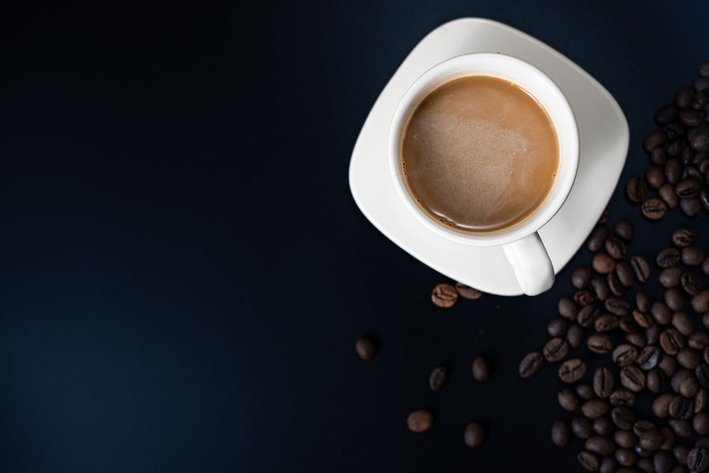 Flat lay of a cup of coffee with coffee beans on a dark background