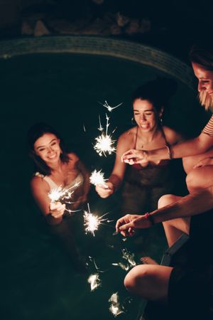 Cheerful friends burning sparkles near pool