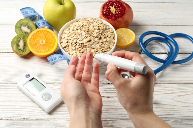 Female checking blood sugar level on background with diabetic accessories